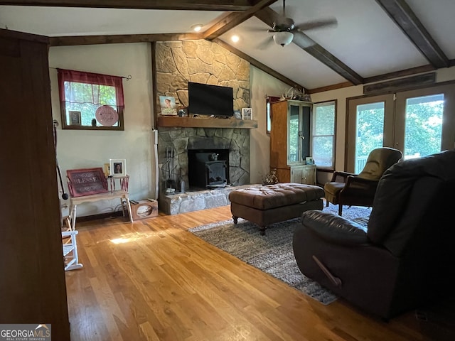 living room featuring a stone fireplace, wood-type flooring, vaulted ceiling with beams, and ceiling fan