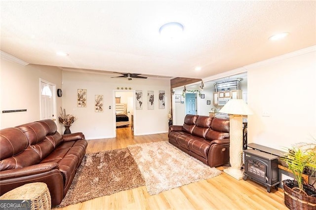 living room with ornamental molding, a wood stove, light hardwood / wood-style floors, and ceiling fan