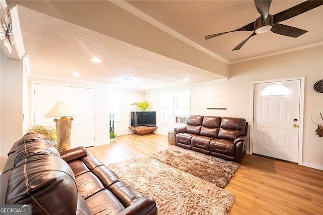 living room featuring ceiling fan, a textured ceiling, ornamental molding, and hardwood / wood-style flooring