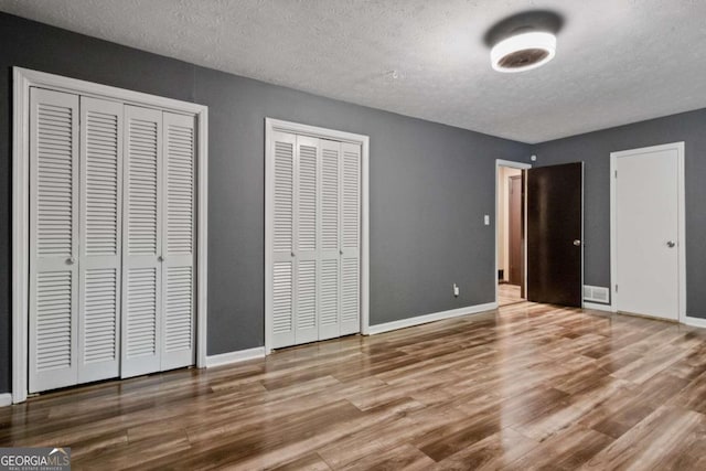 unfurnished bedroom featuring wood-type flooring, two closets, and a textured ceiling