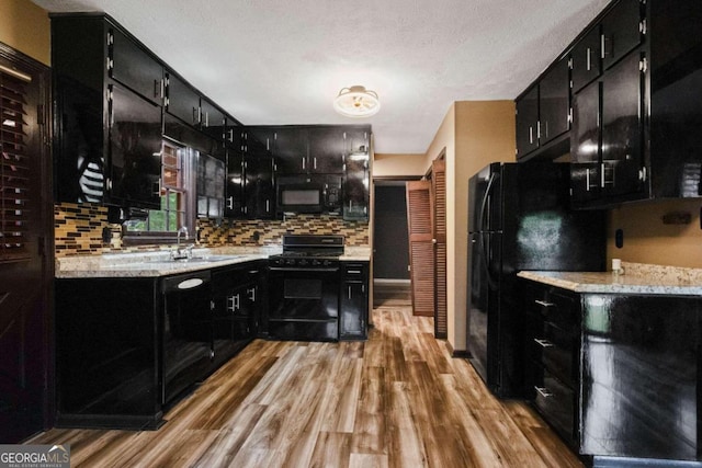 kitchen with decorative backsplash, light hardwood / wood-style floors, a textured ceiling, black appliances, and sink