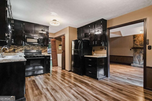 kitchen featuring a textured ceiling, light wood-type flooring, sink, and black appliances