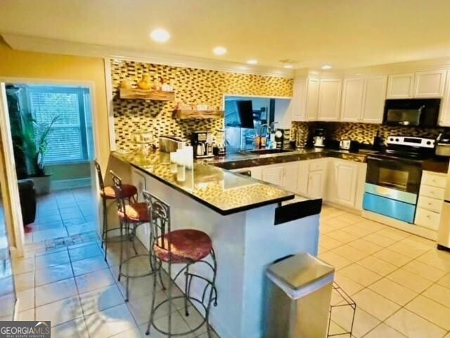 kitchen with kitchen peninsula, white cabinetry, a breakfast bar area, and stainless steel range