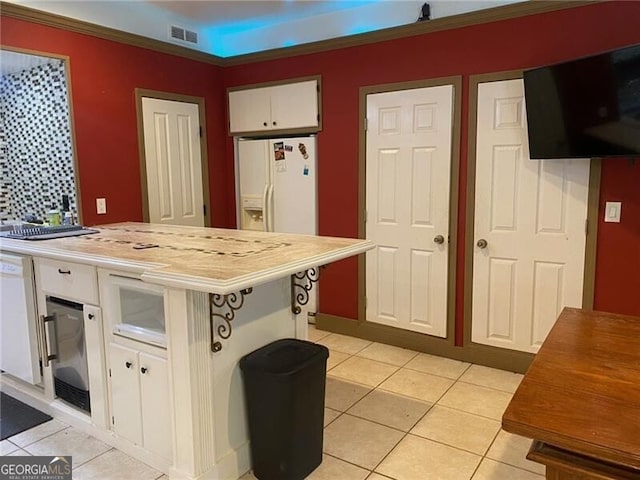 kitchen featuring light tile patterned floors, white cabinetry, white refrigerator with ice dispenser, a breakfast bar area, and crown molding