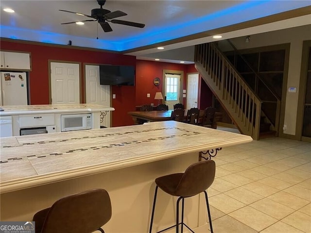 kitchen with white cabinetry, light tile patterned flooring, white appliances, a kitchen bar, and ceiling fan