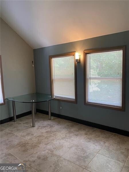 tiled empty room featuring vaulted ceiling