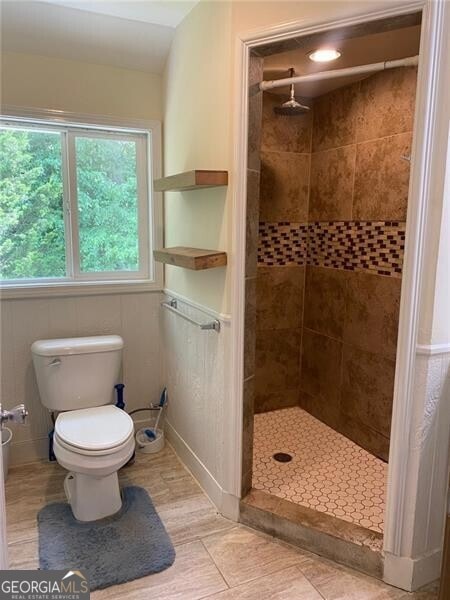 bathroom with wood-type flooring, toilet, and tiled shower