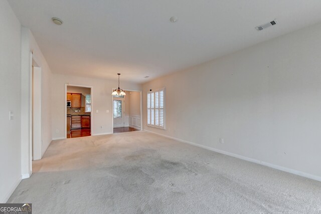 unfurnished living room featuring a chandelier and light colored carpet