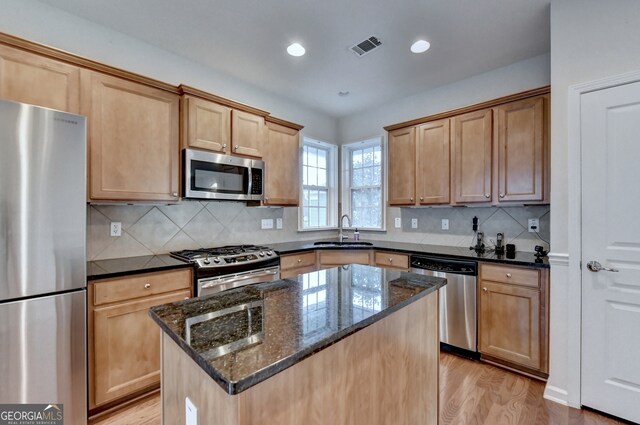 kitchen featuring sink, stainless steel appliances, a center island, dark stone countertops, and light wood-type flooring