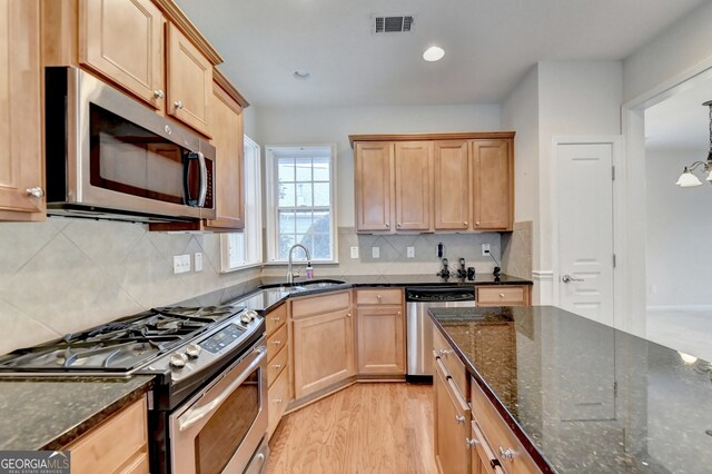 kitchen with hanging light fixtures, light hardwood / wood-style flooring, appliances with stainless steel finishes, dark stone counters, and decorative backsplash