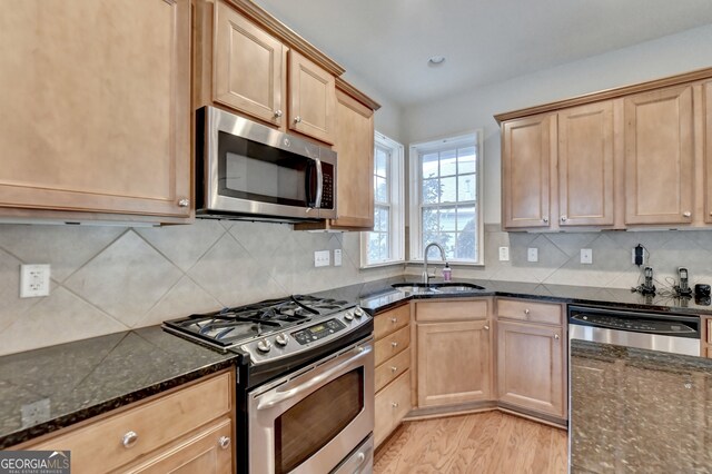 kitchen featuring appliances with stainless steel finishes, light hardwood / wood-style floors, dark stone countertops, backsplash, and sink