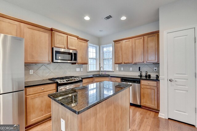 kitchen featuring dark stone counters, a center island, sink, light hardwood / wood-style flooring, and stainless steel appliances