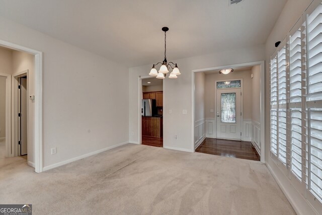 unfurnished room featuring light colored carpet, an inviting chandelier, and a wealth of natural light