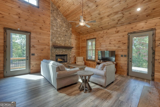 living room with ceiling fan, wood walls, light hardwood / wood-style floors, and high vaulted ceiling