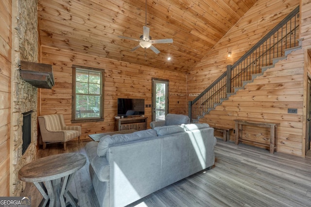 living room with high vaulted ceiling, a stone fireplace, wood walls, wood-type flooring, and ceiling fan