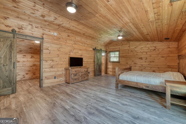 unfurnished bedroom featuring wood-type flooring, vaulted ceiling, wood walls, and a barn door