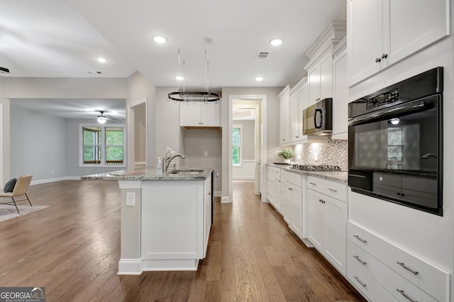 kitchen featuring light stone counters, sink, a kitchen island with sink, white cabinetry, and dark hardwood / wood-style floors