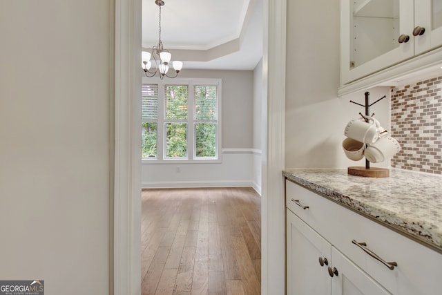 bar featuring light stone counters, white cabinets, backsplash, wood-type flooring, and decorative light fixtures