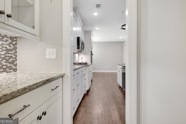 kitchen with light stone counters, tasteful backsplash, white cabinetry, stainless steel appliances, and dark hardwood / wood-style flooring