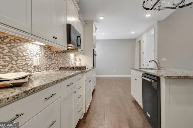 kitchen featuring white cabinetry, light stone countertops, stainless steel appliances, wood-type flooring, and sink