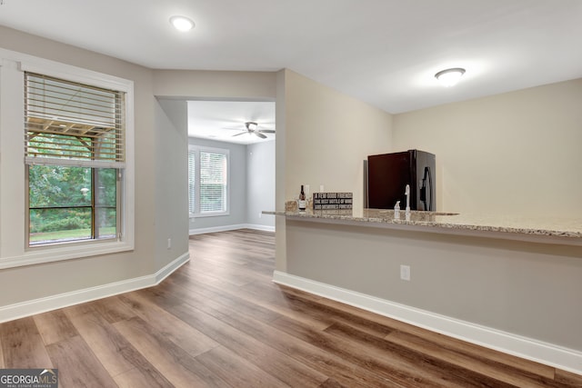 kitchen featuring ceiling fan, black fridge, hardwood / wood-style flooring, and light stone countertops