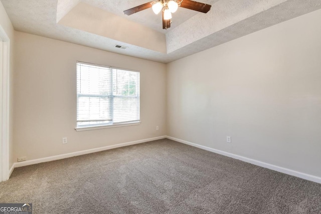 carpeted spare room featuring a textured ceiling, a tray ceiling, and ceiling fan