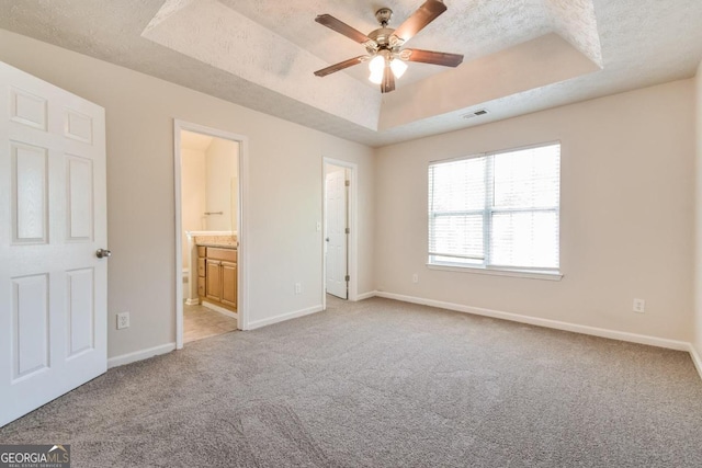 unfurnished bedroom featuring a tray ceiling, a textured ceiling, ensuite bathroom, and ceiling fan