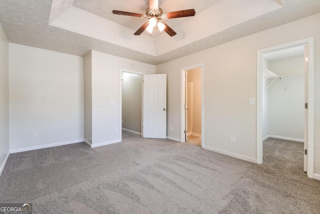 unfurnished bedroom featuring a closet, a textured ceiling, ceiling fan, a walk in closet, and light colored carpet