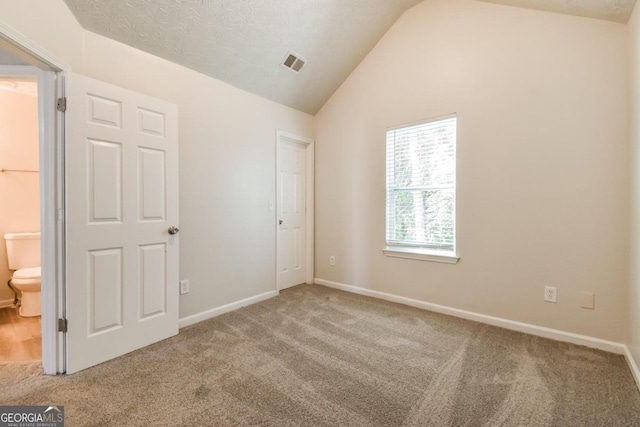 unfurnished bedroom with a textured ceiling, lofted ceiling, connected bathroom, and carpet