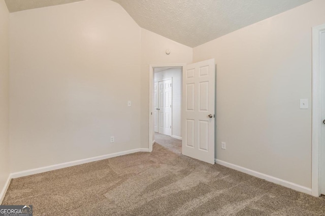 spare room with vaulted ceiling, a textured ceiling, and carpet flooring