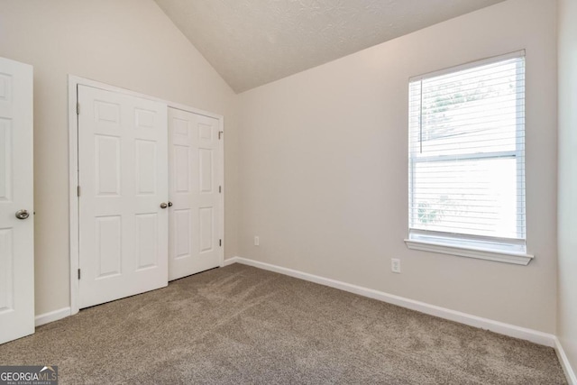 unfurnished bedroom with a textured ceiling, lofted ceiling, and light carpet