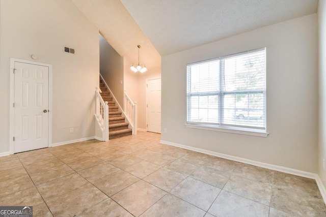 empty room with high vaulted ceiling, a textured ceiling, light tile patterned flooring, and an inviting chandelier