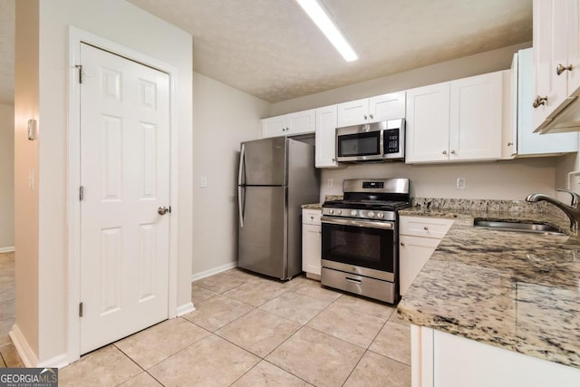 kitchen featuring sink, white cabinets, stainless steel appliances, light tile patterned floors, and light stone countertops