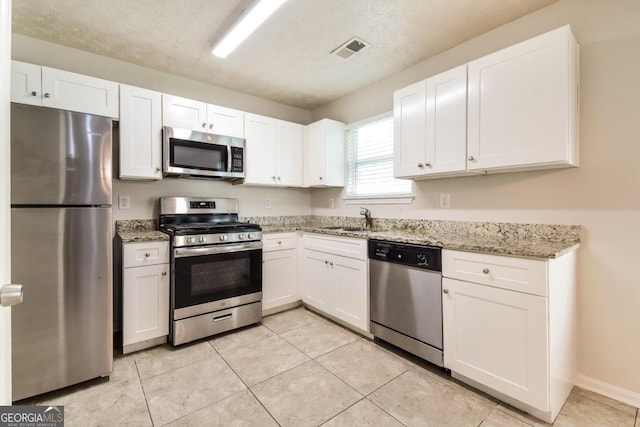 kitchen featuring light tile patterned floors, sink, white cabinetry, appliances with stainless steel finishes, and light stone countertops