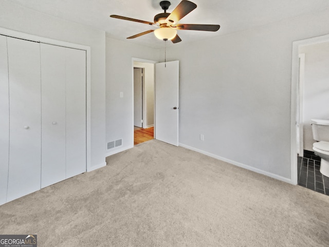 unfurnished bedroom with ceiling fan, light carpet, ensuite bathroom, and a closet