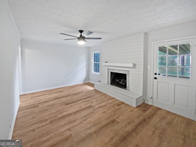 unfurnished living room featuring a textured ceiling, hardwood / wood-style flooring, a brick fireplace, crown molding, and ceiling fan