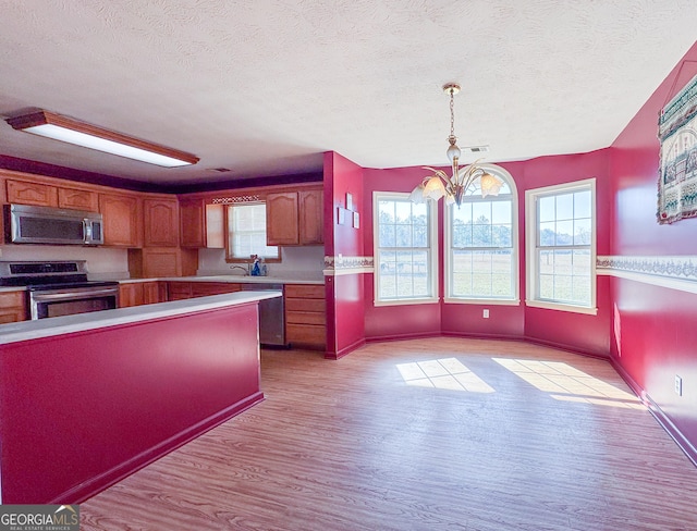 kitchen with an inviting chandelier, decorative light fixtures, a textured ceiling, stainless steel appliances, and light hardwood / wood-style floors