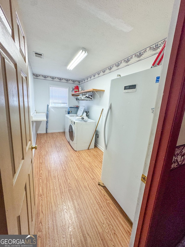 clothes washing area with washing machine and dryer, a textured ceiling, and light hardwood / wood-style flooring