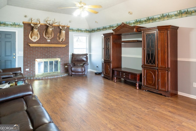 living room with vaulted ceiling, a brick fireplace, wood-type flooring, and ceiling fan