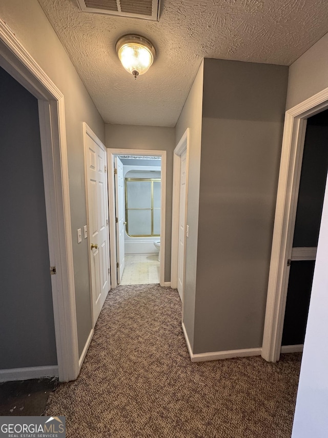 corridor with a textured ceiling and dark colored carpet