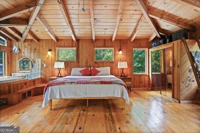 bedroom featuring multiple windows, light hardwood / wood-style floors, and wood walls