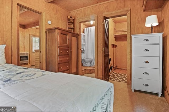 bedroom with carpet floors, heating unit, wood walls, and ensuite bathroom