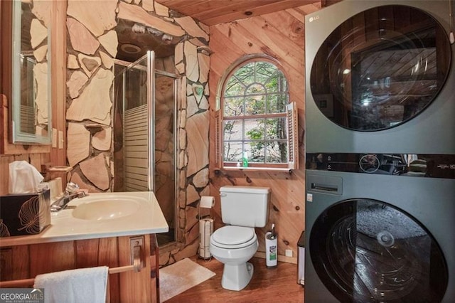 bathroom with stacked washer and dryer, an enclosed shower, wood walls, vanity, and toilet