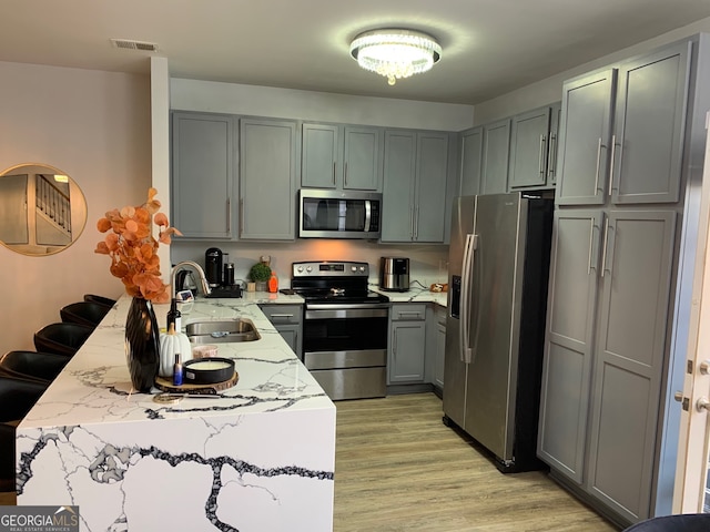 kitchen featuring light wood-type flooring, sink, gray cabinetry, appliances with stainless steel finishes, and light stone countertops