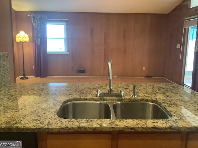 kitchen with wooden walls, light stone countertops, and a sink