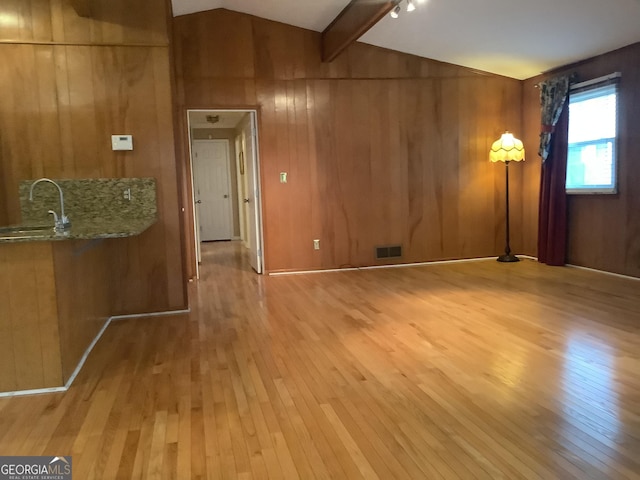 unfurnished room with wooden walls, vaulted ceiling with beams, wood-type flooring, and a sink