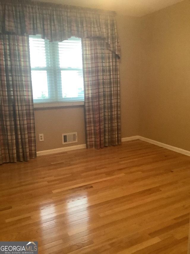 empty room featuring visible vents, baseboards, and wood finished floors