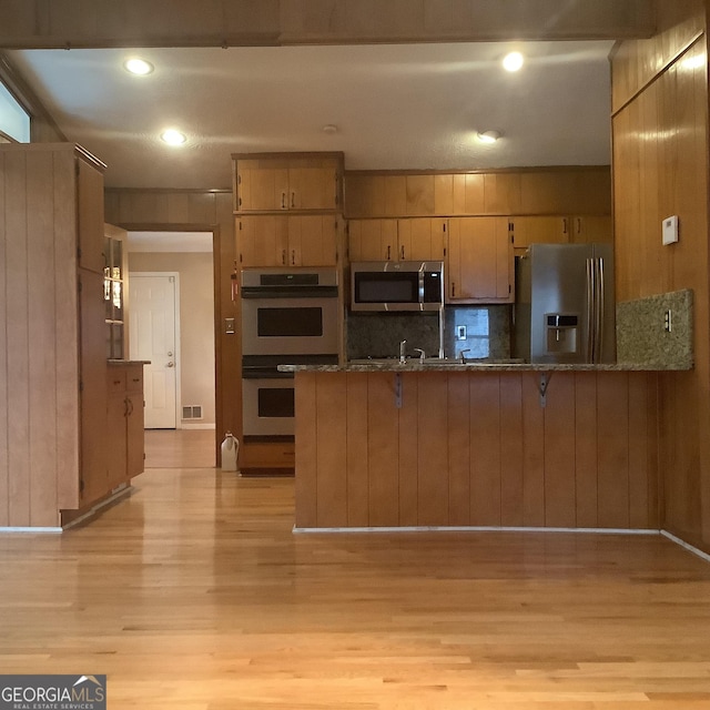 kitchen featuring visible vents, a peninsula, stainless steel appliances, light wood-style floors, and backsplash