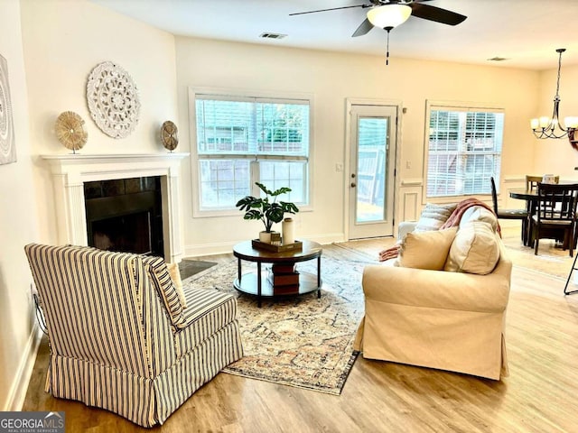 living room featuring hardwood / wood-style flooring, ceiling fan with notable chandelier, a tile fireplace, and a healthy amount of sunlight