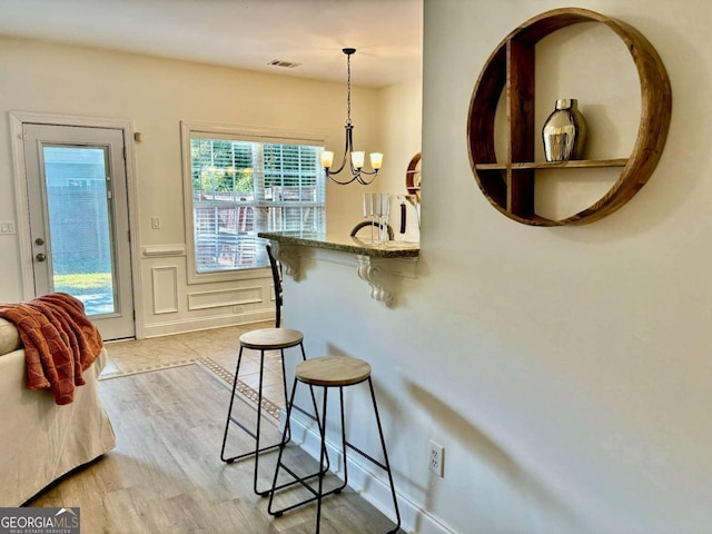 interior space with pendant lighting, light stone counters, light hardwood / wood-style floors, a kitchen breakfast bar, and an inviting chandelier